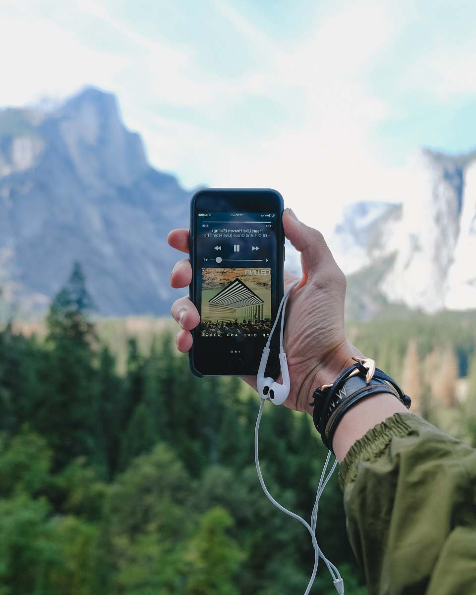 yosemite valley person playing music on space gray iPhone 5s with EarPods on hand during daytime phone